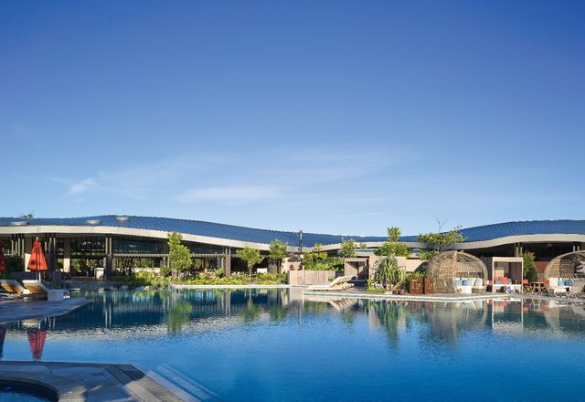 The crescent form of the double curved zinc roof opens up to a large pool, with views to vegetated sand dunes in the distance.