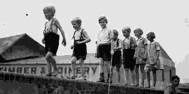 Five small boys and two girls walking along a brick wall, Sydney, ca.1934.