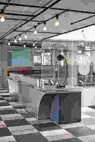 The stainless steel reception desk has a curved cutaway form that reveals a teal finish underneath, complementing the vinyl terrazzo flooring.