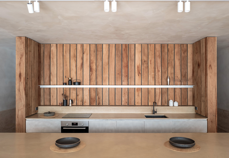 یک دیوار چوبی که آشپزخانه را در خود جای داده است، یک قفسه کتاب برای فضاهای نشیمن تشکیل می دهد.