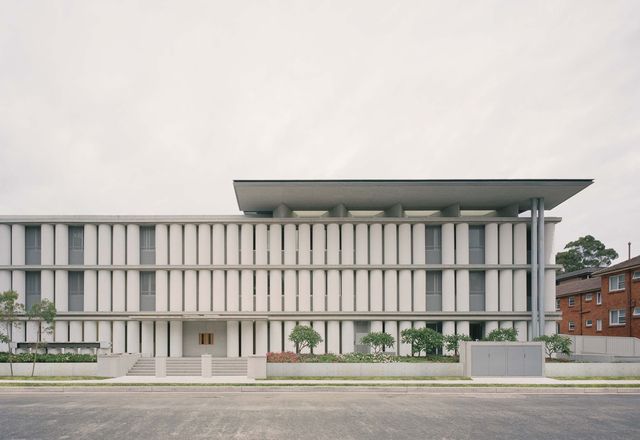 The facade’s half-pipe concrete pillars reduce sight lines into the building, while their matt white finish holds and softly reflects light.