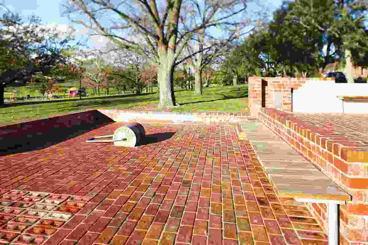 A steel tennis court roller is fixed into the brick paving – a reminder of the site’s former life.
