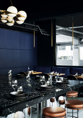 A generous communal table topped with nero marquina herringbone tiles anchors the open-plan space, drawing visitors to congregate centrally.