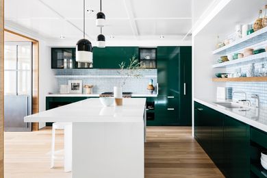 Green enamel cabinetry is dark and rich in contrast to the white tile splashback in the spacious, comfortable kitchen.