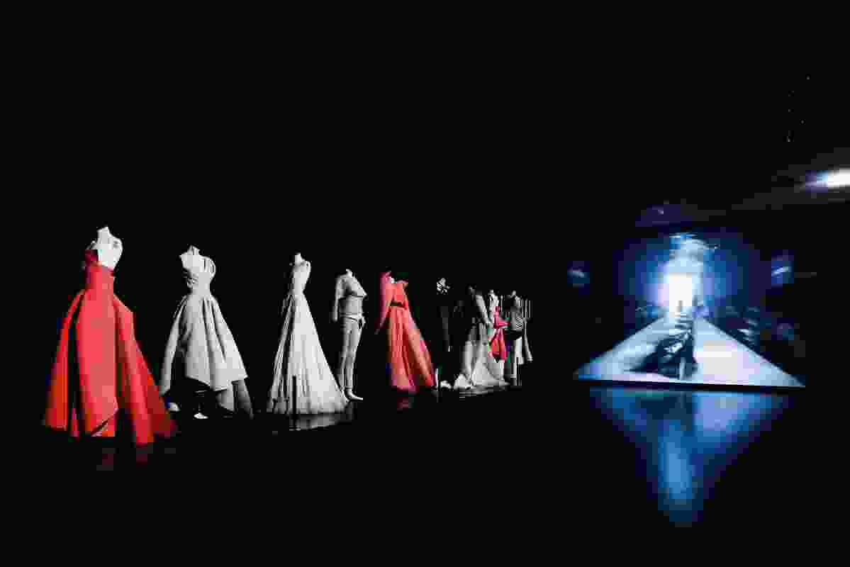 Theatrical lighting shines down on the gowns, making them pop in the dark space.