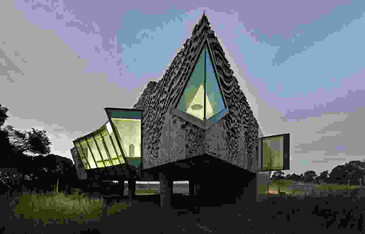 The exterior form features abrupt, beak-like gable ends; slung suspended roof lines; a pachydermatous concrete panel system; and bulbous, tapered, table-leg columns.