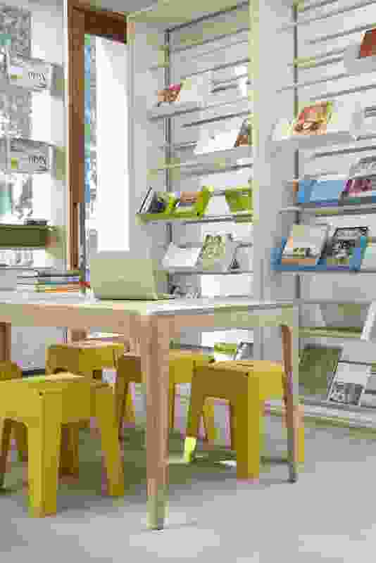 The library space includes shelving in blonde timber with a matching table and yellow stools.