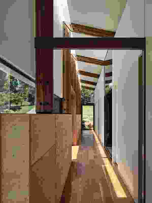Slots of sashless glazing sit between the rammed earth wall and the folded roof line; sections of the wall push out into day beds or small porches.