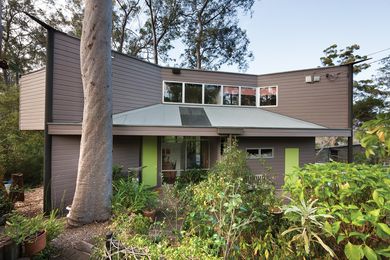 A flat-topped weatherboard wall sits between steel posts exposed at the corners, giving the house a crisp profile on approach.